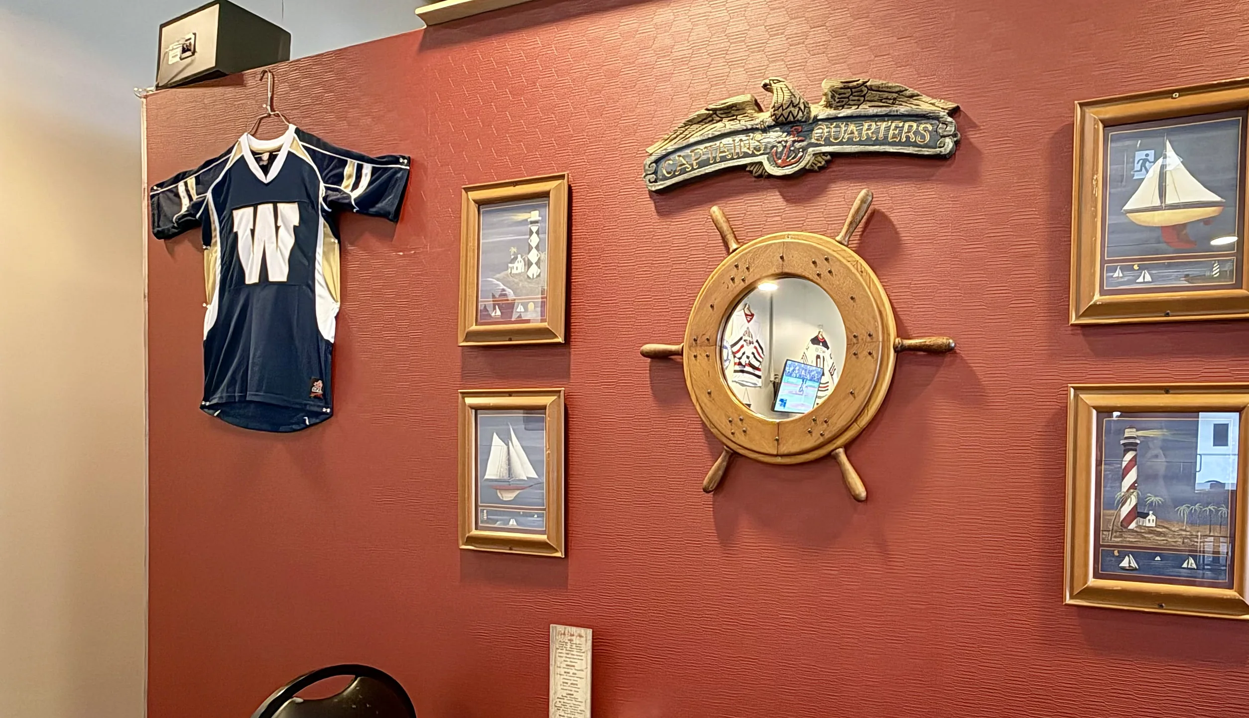 Riverboat dining room wall with a ship's wheel, sailboat pictures and a football jersey