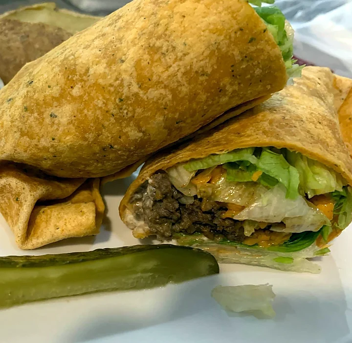 Beef taco wrap cut in half with a pickle spear