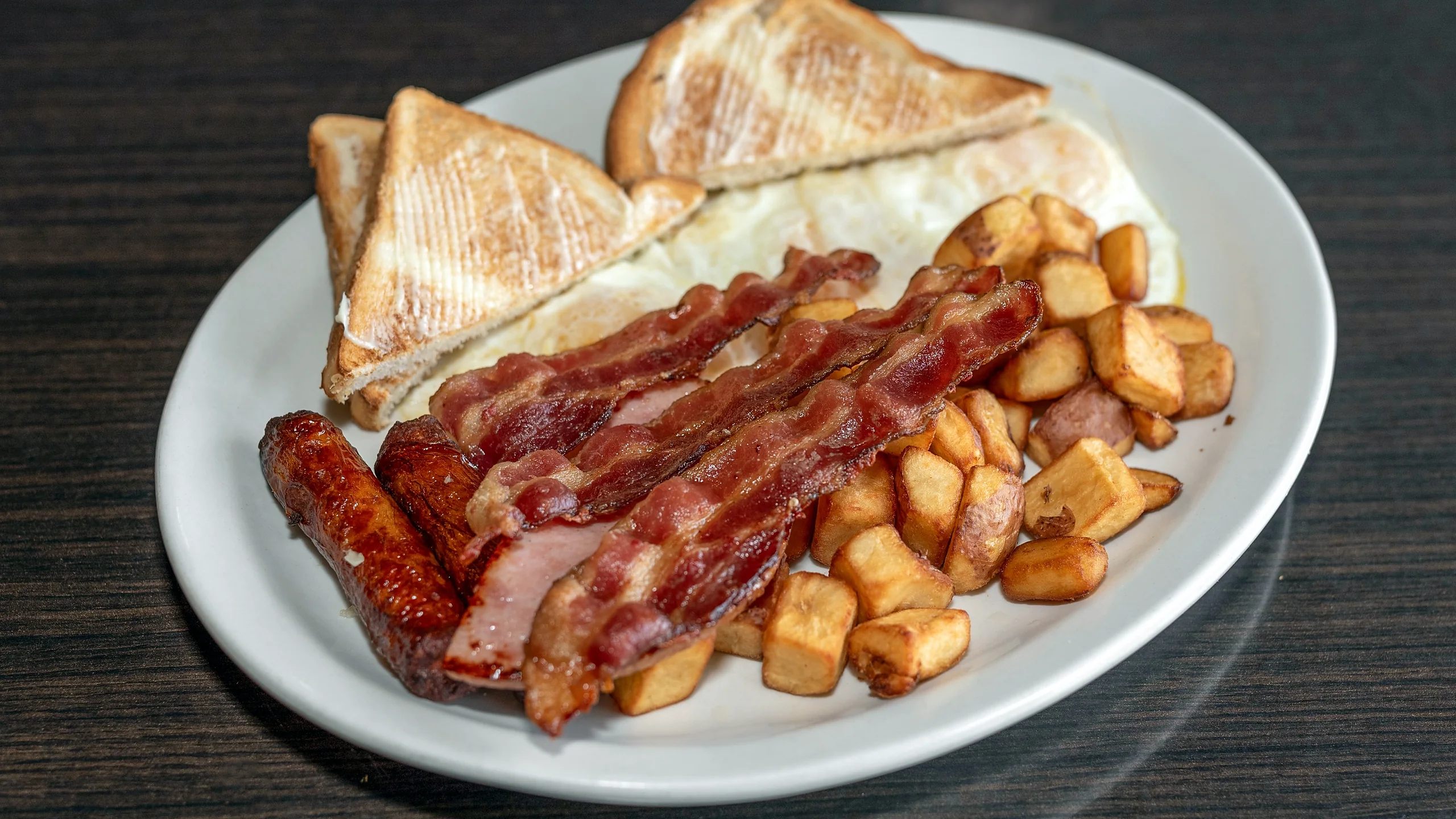 Breakfast plate with bacon, sausage, eggs, home fries and toast