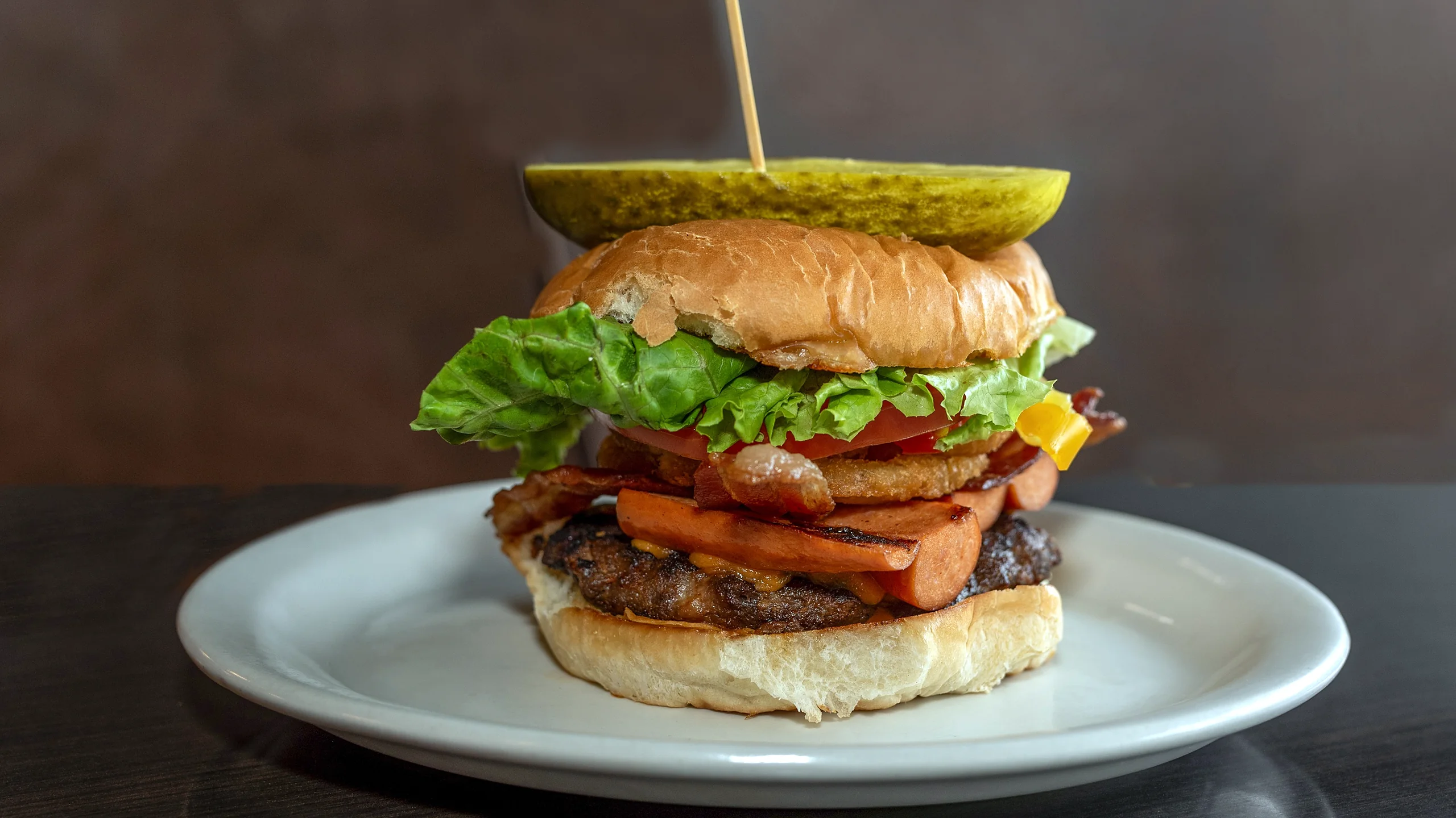Burger with bacon, cheese, tomato and lettuce, topped with a pickle spear