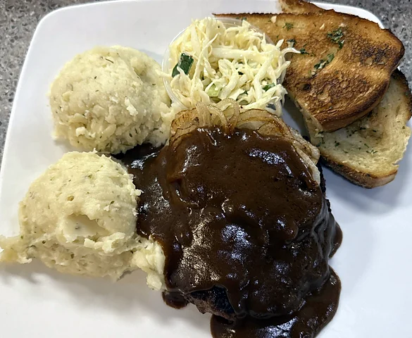 Hamburger steak in gravy with mashed potatoes, coleslaw and garlic toast